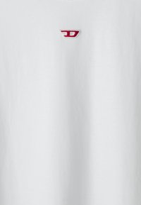 Hvit bomulls T-skjorte med korte ermer, med en liten rød brodert logo på øvre venstre side. Glatt tekstur, enkelt design.