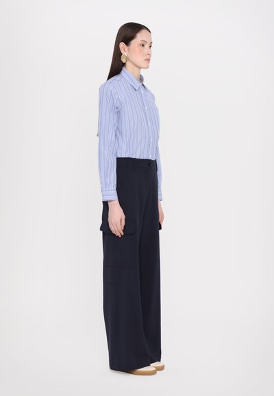 Chemise à rayures bleues et blanches à boutons avec col, associée à un pantalon cargo taille haute navy avec poches latérales et jambes larges.