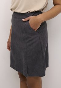 Jupe grise avec une texture lisse, poches latérales et une coupe droite. Présente une taille ajustée et une petite fente à l'ourlet.