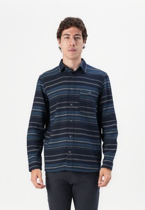 Camisa de botones azul a rayas con cuello y bolsillo en el pecho, con diferentes tonalidades de azul y gris sobre un fondo oscuro.