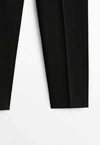 Pantalon noir à jambes droites étalé à plat sur fond blanc, montrant les ourlets et les parties inférieures des jambes.