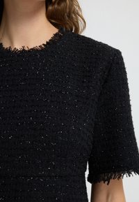 Mustat teksturoidut mekko, jossa on löysä istuvuus, fringe-tyylinen kaula-aukko ja lyhyet hihat. Pienet hopealangat tuovat hienovaraisia yksityiskohtia kankaaseen.