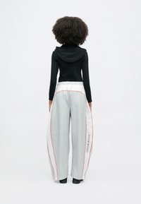 Jasnoszare luźne spodnie z czerwonym paskiem i napisem „NIKE SHOX”, zestawione z czarną bluzą z długim rękawem i kapturem.