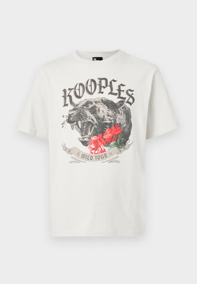 Λευκό T-shirt με μια βρυχώμενη μαύρη πάνθηρα, κόκκινα λουλούδια, το κείμενο "KOOPLES" πάνω και ένα πανό "WILD TOUR" κάτω από το γραφικό στο κέντρο μπροστά.