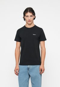 Tricou din bumbac negru cu mâneci scurte, decolteu rotund și logo alb pe piept. Asortat cu blugi din denim de culoare albastru deschis.