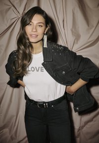 Crna traper jakna s ukrasnim detaljima na ramenima, bijela majica s natpisom "LOVE" od srebrnih zakovica, uparen s tamnim trapericama i crnim remenom.
