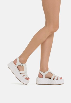 White platform sandals with multiple straps and an adjustable ankle buckle. Textured sole with woven pattern. Smooth, matte finish.