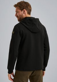 Sudadera con capucha negra de acabado texturizado, con mangas largas y un parche del logotipo en el hombro izquierdo.