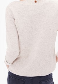 Pull beige à la texture douce, avec un col rond et des manches trois-quarts. Un petit bouton marron orne le dos.