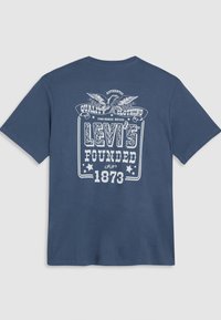 Tamsiai mėlynos spalvos medvilninis marškinėlis su baltu spausdintu dizainu. Tekstas apima "Levi's" ir "Įkurtas 1873", su dekoratyviniais elementais ir ereliu.