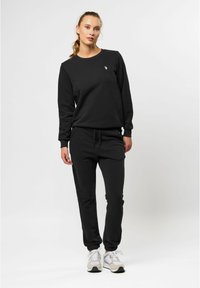 Svart sweatshirt och joggers i mjukt material med ribbade muddar. Har en liten logotyp på sweatshirten. Kombineras med sneakers i neutrala färger.