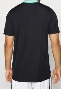 Czarny sportowy t-shirt z turkusowym kołnierzykiem, krótkimi rękawami i prostym dołem. Materiał wydaje się gładki, bez widocznych wzorów ani grafik.
