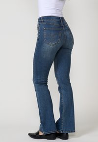 Jeans de mezclilla azul de pernera acampanada con una cintura alta, costuras decorativas en los bolsillos traseros y una textura suave. Ajuste casual con un ligero estiramiento.