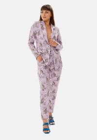 Pink patterned suit featuring leopards and spots, tailored fit, single-button blazer, and matching tapered trousers, paired with blue sandals.