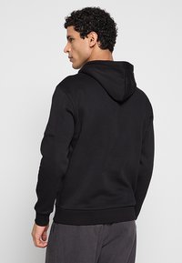 Zwarte hoodie met een gestructureerde afwerking, capuchon met trekkoord en geribbelde manchetten. Heeft een eenvoudig ontwerp, zichtbare stiksels en een comfortabele pasvorm.