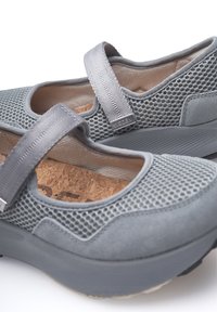 Zapatillas de malla grises con un acabado de ante suave, una correa en la parte superior y una plantilla de corcho texturizada. Presenta una suela de goma ligera.