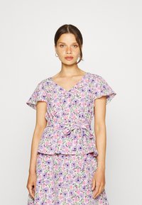 Top com estampa floral, com mangas curtas tipo "flutter", tecido leve, decote em v, cintura ajustada com um cinto, apresentando flores roxas e rosas.