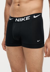 Ανδρικός κορμός με μαύρα boxer Nike με λευκό λογότυπο στη μέση και στο πόδι, με ορατό τρύπημα στον ομφαλό.