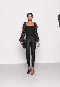 Top negro ajustado con mangas abullonadas de tul con lunares, combinado con jeans skinny negros de tiro alto y sandalias de tacón negro con tiras.
