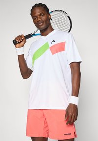 Hvid tennis skjorte med grønne og lyserøde geometriske accenter, parret med koralfarvede shorts. Inkluderer en tennisracket og håndledsbånd.