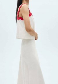 Top blanco sin mangas con acentos rojos en forma de concha, combinado con una falda blanca ajustada y larga hasta el suelo. Tejido suave con una textura sutil.