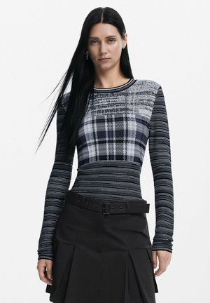 Maglietta a maniche lunghe con motivi a righe e a quadri in tonalità di nero e grigio, realizzata in un tessuto a maglia testurizzato. Abbinata a una gonna nera e a una cintura.
