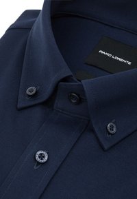 Granatowa koszula z teksturowanej tkaniny, z wyokrąglonym kołnierzykiem i dwoma okrągłymi guzikami z ciemnymi akcentami, oznaczona napisem "PAKO LORENTE."