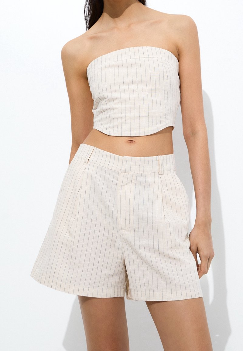 Crop top beige senza maniche e pantaloni corti abbinati, con strisce blu verticali, vestibilità su misura e superficie liscia.