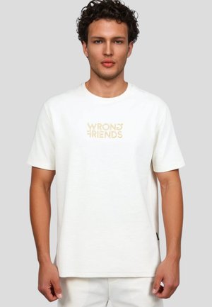 Camiseta blanca de manga corta hecha de algodón suave, con el logotipo bordado "WRONG FRIENDS" en beige en el centro. Ajuste simple y relajado.