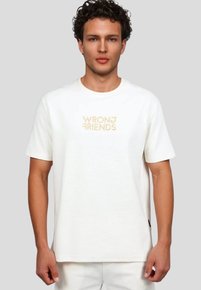 Camiseta blanca de manga corta hecha de algodón suave, con el logotipo bordado "WRONG FRIENDS" en beige en el centro. Ajuste simple y relajado.