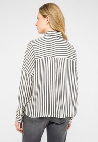 Blusa a rayas en crema y marino, con cuello, mangas largas y una abertura en la espalda. Corte suelto con una textura suave y detalles mínimos.