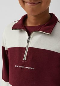 Bordeaux- und weiße gestreifte Zip-up-Sweatshirt mit strukturiertem Rippmaterial, ausgestattet mit einem hohen Kragen und gesticktem Logo auf der Brust.