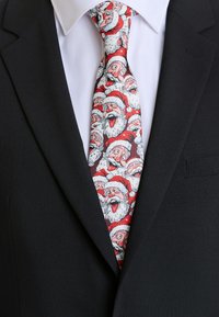 Cravatta da uomo con un motivo fantasioso di volti di Babbo Natale in rosso, bianco e nero su un tessuto testurizzato, indossata con un abito scuro.