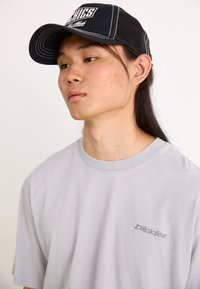 T-shirt cinza de algodão com mangas curtas e gola redonda, apresentando um logótipo bordado discreto. Boné de malha preto com um design gráfico.