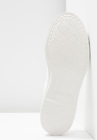 Suola di sneaker in gomma bianca con un motivo testurizzato e il logo del marchio "B" sul tallone. Design pulito con bordi lisci e profilo piatto.