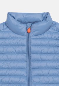 Ανοιχτό μπλε μπουφάν καπιτονέ με ψηλό γιακά και φερμουάρ μπροστά με πορτοκαλί τράβηγμα.