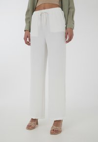 Pantaloni bianchi a gamba larga con un tessuto testurizzato e una vita elastica, abbinati a tacchi beige con cinturini.