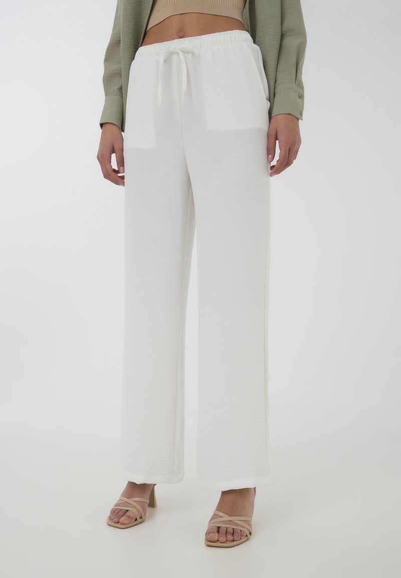 Pantaloni bianchi a gamba larga con un tessuto testurizzato e una vita elastica, abbinati a tacchi beige con cinturini.