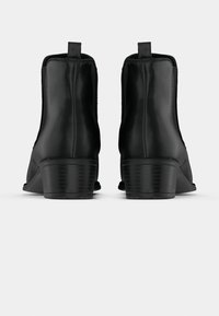 Botines negros hasta el tobillo hechos de cuero liso con un tacón bajo y apilado, que cuentan con paneles laterales elásticos y una lengüeta para facilitar su colocación.