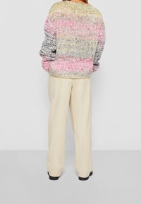 Pull en maille multicolore avec des rayures roses, grises et jaunes, coupe décontractée et poignets côtelés. Associé à un pantalon large crème.