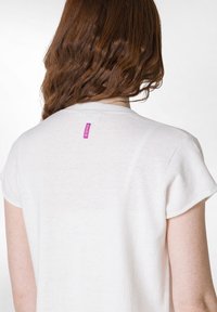 Weißes Kurzarmhemd aus weichem Material mit einem kleinen rosa Etikett, auf dem "DEHA" steht, das sich am Nacken des Rückens befindet.