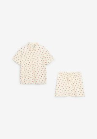Set di camicia a maniche corte con bottoni e pantaloni corti in crema, con una fantasia di piccoli cuori rossi su tutta la superficie. I pantaloni corti presentano una vita elastica con cordoncino.