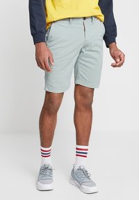 Pantalones cortos azul claro con un corte clásico, hechos de tela de algodón, con bolsillos laterales y cierre de botón. Combinados con zapatillas grises y calcetines a rayas.