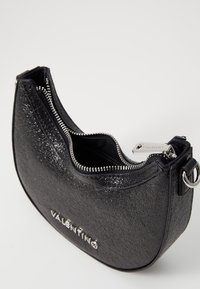 Borsa in pelle nera con finitura testurizzata, zip argentata e logo VALENTINO; forma ovale con manico corto e design aperto.