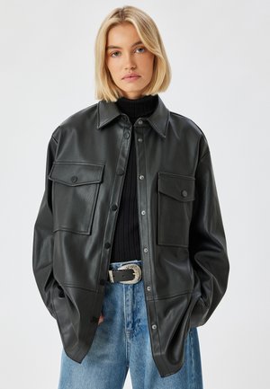 Zwarte leren oversized jas met knopen, twee borstzakken en een gladde textuur, gecombineerd met een zwarte geribbelde coltrui en blauwe jeans.