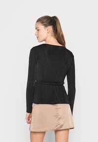 Top preto de mangas compridas com uma cintura ajustada e design peplum, feito de um tecido brilhante. Combinado com uma saia de cetim bege claro, com costura lateral.