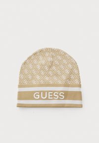 Bež kapica pletena s ponavljajućim uzorkom loga i bijelim trakama na kojima je istaknuto ime brenda "GUESS".