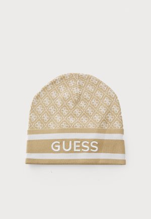 Beige strikket lue med gjentakende logo-mønster og en hvit reim med merkevarenavnet "GUESS" tydelig vist.