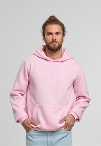 Sudadera de color rosa claro con un gran bolsillo frontal, capucha con cordones y puños de canalé. Combinada con jeans de denim claros, creando un look casual.