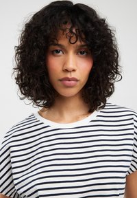 Balta marškinėliai su tamsiai mėlynomis horizontaliomis juostelėmis, apvalia iškirpte ir trumpomis rankovėmis. Minkšta medžiaga su laisvu kirpimu ir matomomis siūlėmis.